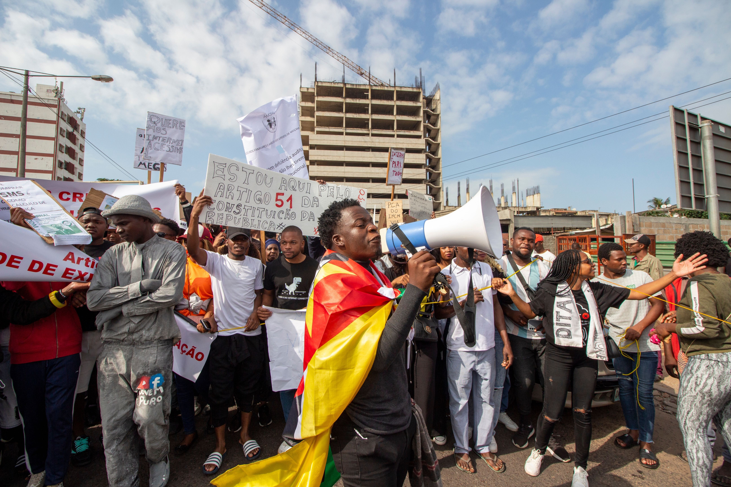 Maputo, Mozambique - 18 mai 2024  : Un homme vêtu d'un drapeau mozambicain  adresse la foule d'un mégaphone lors d'une manifestation, tandis que les participants tiennent des bannières dans  assistance de leur cause