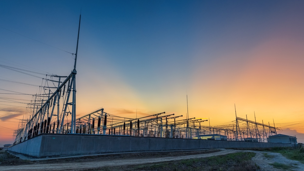power substation with transformers, insulators, and overhead lines silhouetted against a sunset sky