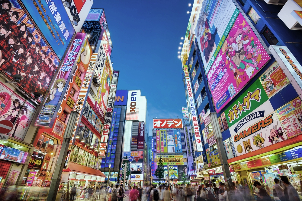 TOKYO, JAPAN - AUGUST 1, 2015: Crowds pass below colorful signs in Akihabara