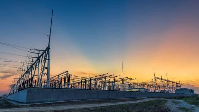 power substation with transformers, insulators, and overhead lines silhouetted against a sunset sky
