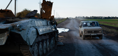 A vehicle with the sign “+”, markings often found on Ukrainian army vehicles, seen driving past a destroyed tank with the sign “Z”, markings often found on Russian military vehicles near the border of Kharkiv and Donetsk region, 2022. 