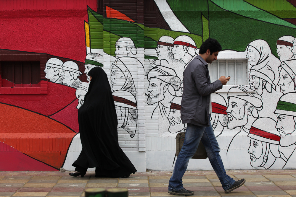 TEHRAN, IRAN - APRIL 3, 2012: People walking in Imam Khomeini Street with street art wall in background